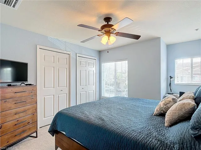 Carpeted bedroom with a textured ceiling, ceiling fan, and multiple closets
