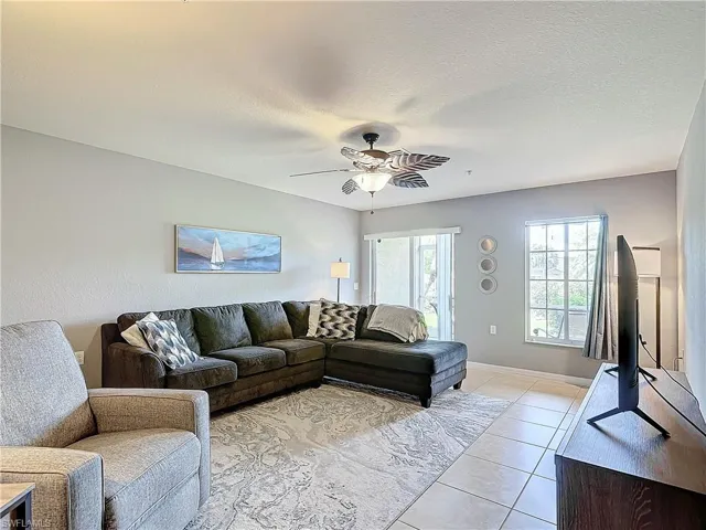 Living room with ceiling fan, a textured ceiling, and light tile patterned flooring