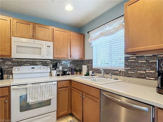 Kitchen with backsplash, sink, light tile patterned floors, and white appliances