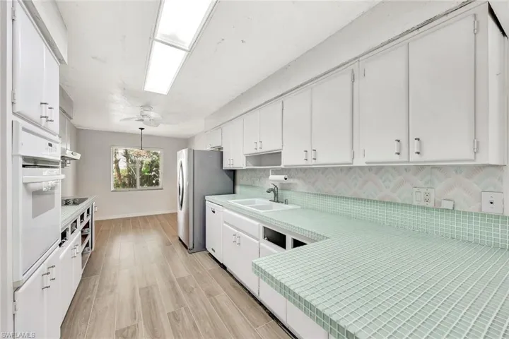 Kitchen with white cabinets, light wood finished floors, light countertops, white appliances, and a sink