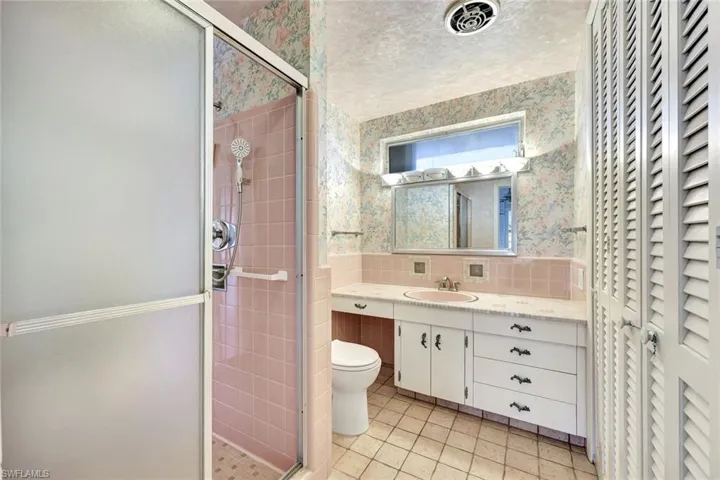 Bathroom featuring wallpapered walls, a stall shower, vanity, tile walls, and tile patterned flooring