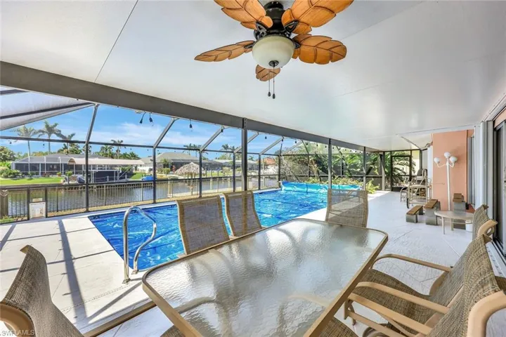 Pool featuring glass enclosure, a ceiling fan, a patio, and a water view
