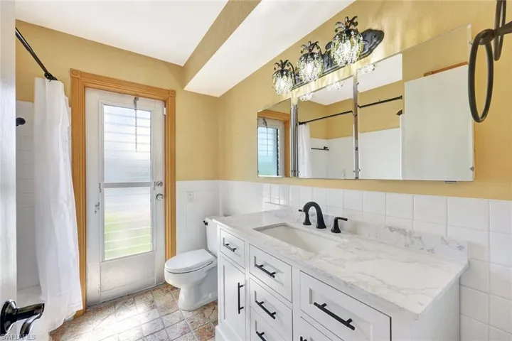 Bathroom with curtained shower, a wainscoted wall, toilet, vanity, and tile walls