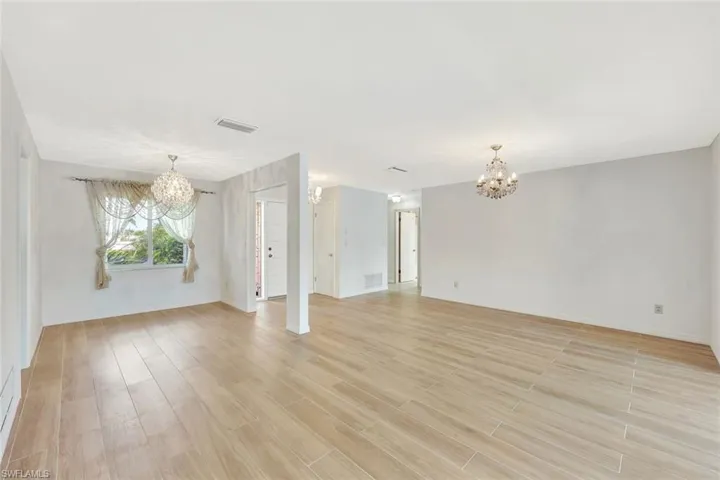 Unfurnished living room with visible vents, light wood-style floors, and a chandelier