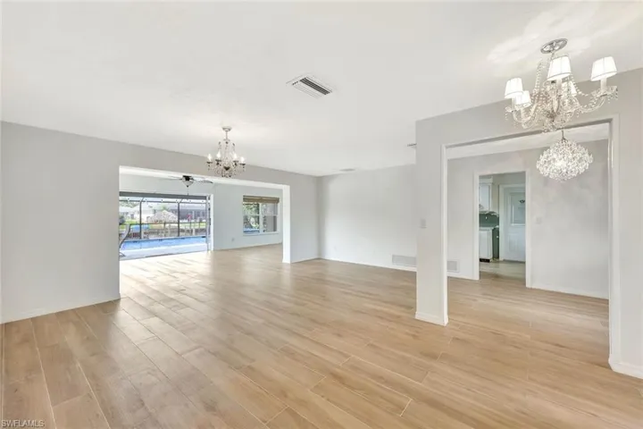 Unfurnished living room featuring light wood finished floors, baseboards, visible vents, and an inviting chandelier