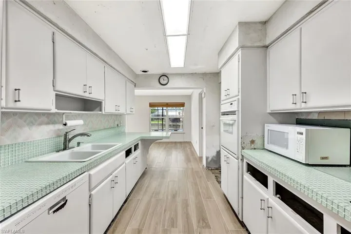 Kitchen featuring light countertops, white cabinets, a sink, and white appliances