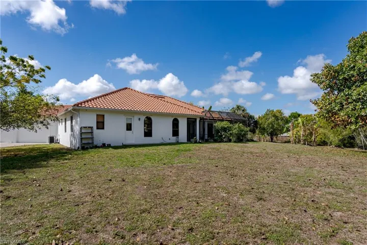 Rear view of house featuring stucco siding, a tile roof, a lanai, and a yard