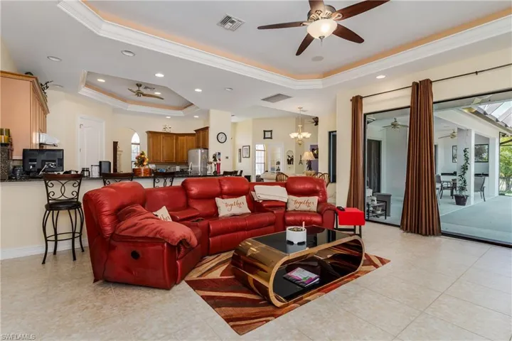 Living area featuring ceiling fan, ornamental molding, arched walkways, a raised ceiling, and suspended lighting