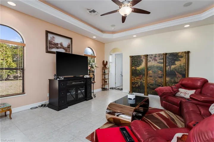 Living area with arched walkways, ceiling fan, a raised ceiling, recessed lighting, and healthy amount of natural light
