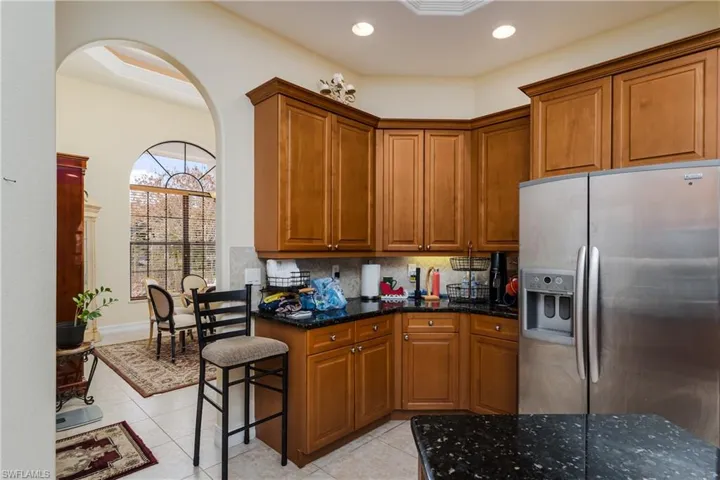 Kitchen with stainless steel fridge, wood finish cabinetry, dark stone counters, backsplash, and light tile patterned flooring