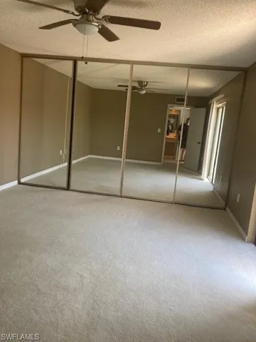 Empty room with a textured ceiling, carpet flooring, and ceiling fan