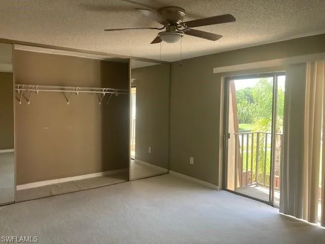 Unfurnished bedroom featuring a closet, access to outside, ceiling fan, carpet floors, and a textured ceiling