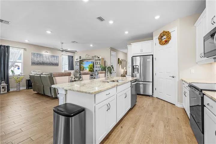 Kitchen featuring white cabinets, light stone counters, stainless steel appliances, open floor plan, and light wood-type flooring