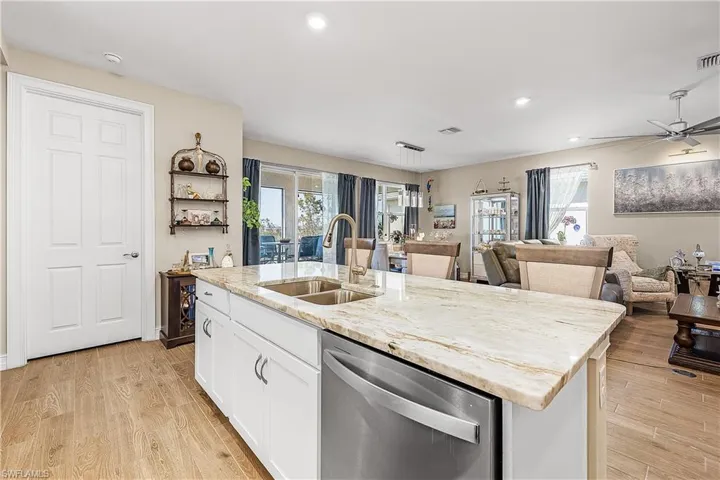 Kitchen with white cabinets, stainless steel dishwasher, open floor plan, light wood-style floors, and light stone counters