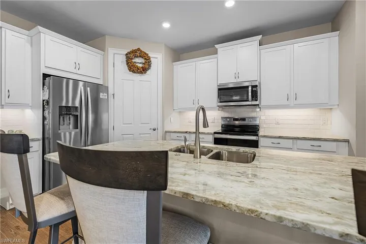 Kitchen with backsplash, white cabinetry, stainless steel appliances, light stone countertops, and recessed lighting