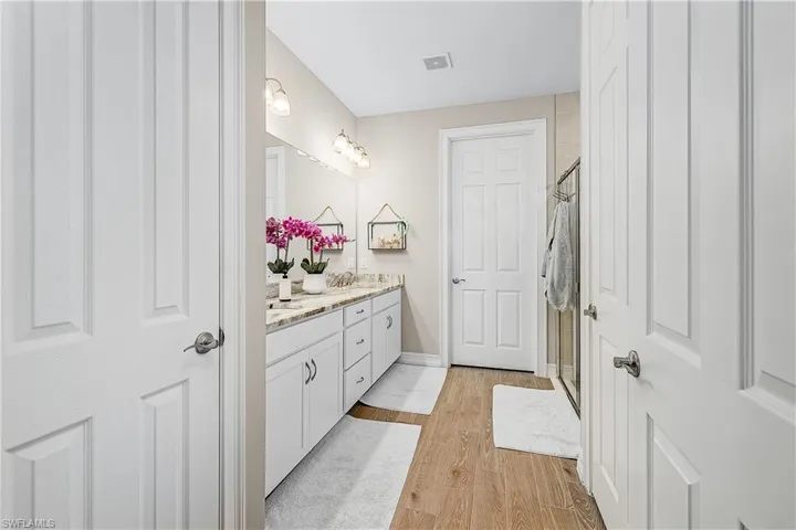 Primary bathroom featuring a shower stall, double vanity, and light wood-type flooring