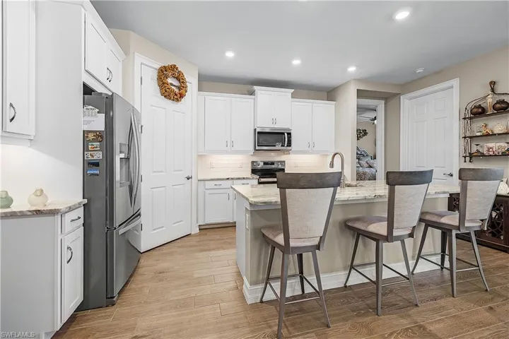 Kitchen with stainless steel appliances, white cabinets, light stone countertops, an island with sink, and light wood-type flooring