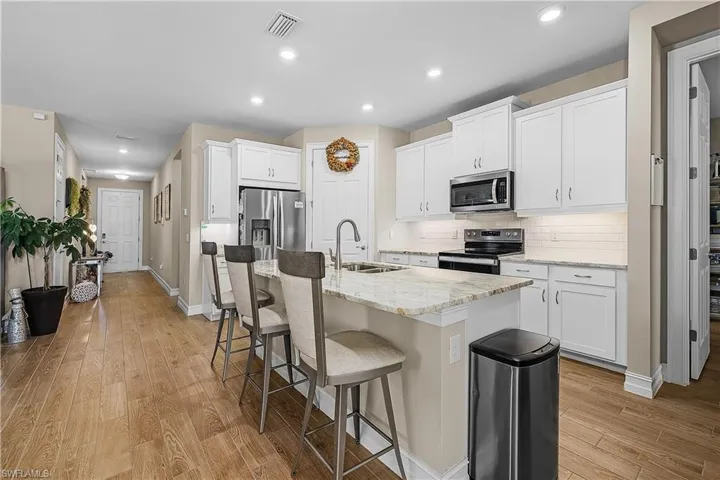 Kitchen featuring white cabinets, stainless steel appliances, light stone countertops, a breakfast bar, and a center island with sink