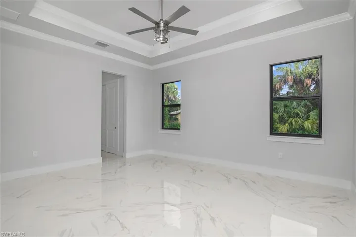 Empty room with ornamental molding, a ceiling fan, light marble finish flooring, and a tray ceiling