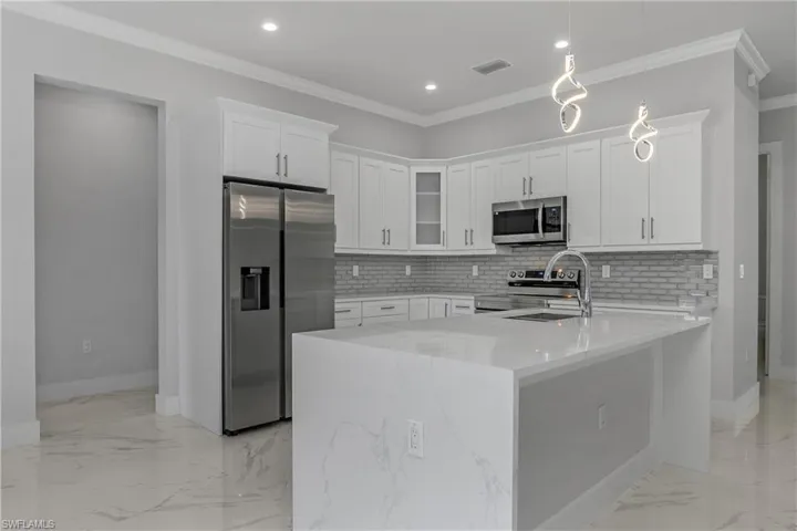Kitchen featuring white cabinets, stainless steel appliances, ornamental molding, light stone counters, and hanging light fixtures