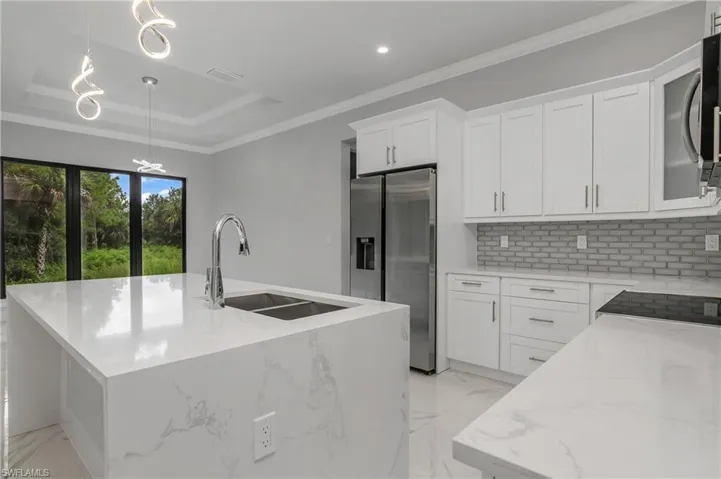 Kitchen with light stone countertops, decorative light fixtures, stainless steel appliances, crown molding, and an island with sink
