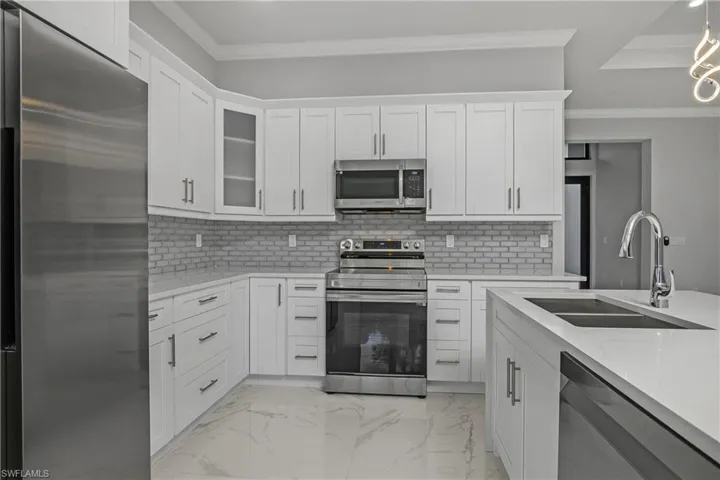 Kitchen featuring stainless steel appliances, ornamental molding, light stone countertops, and white cabinets