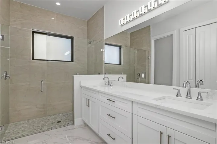 Full bath with a shower stall, double vanity, light marble finish floors, and a closet
