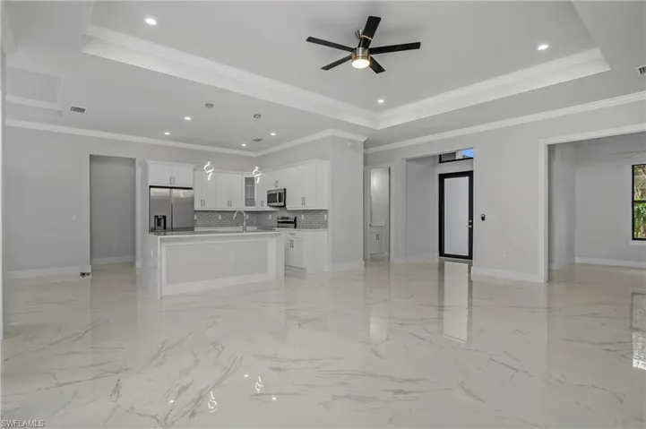 Unfurnished living room with a ceiling fan, ornamental molding, recessed lighting, and a tray ceiling