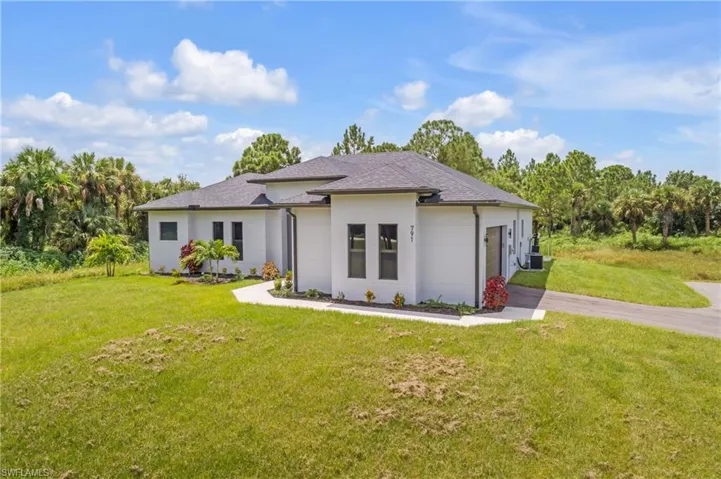 View of front of home with a front yard, driveway, roof with shingles, a garage, and stucco siding