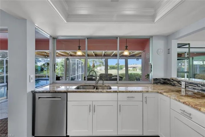 Kitchen featuring stainless steel dishwasher, light stone countertops, a raised ceiling, plenty of natural light, and ornamental molding