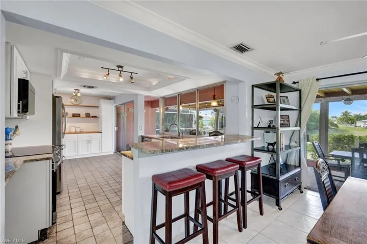 Kitchen featuring ornamental molding, a raised ceiling, white cabinetry, stainless steel appliances, and a kitchen bar