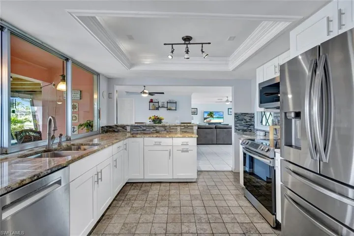 Kitchen with stainless steel appliances, white cabinetry, light stone countertops, a tray ceiling, and open floor plan