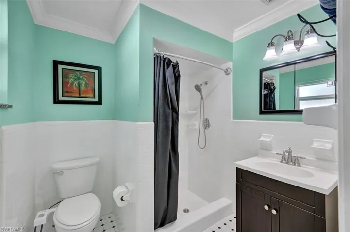 Full bath featuring tile walls, a shower stall, vanity, wainscoting, and ornamental molding