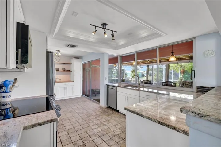 Kitchen featuring white cabinets, a tray ceiling, light stone countertops, crown molding, and stainless steel appliances