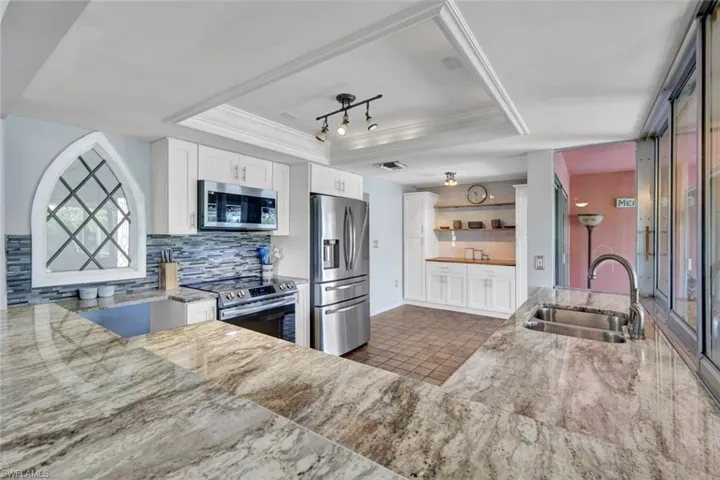 Kitchen with white cabinets, a raised ceiling, stainless steel appliances, backsplash, and light stone countertops