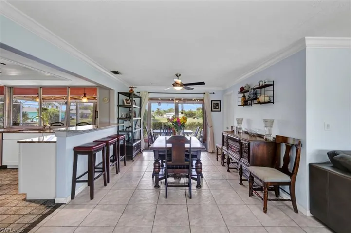 Dining room with ceiling fan, ornamental molding, and light tile patterned floors