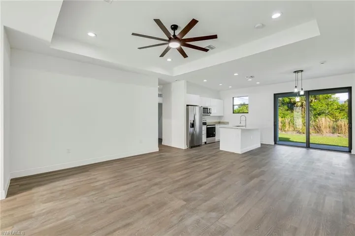 Unfurnished living room featuring sink, light hardwood / wood-style flooring, ceiling fan, and a tray ceiling