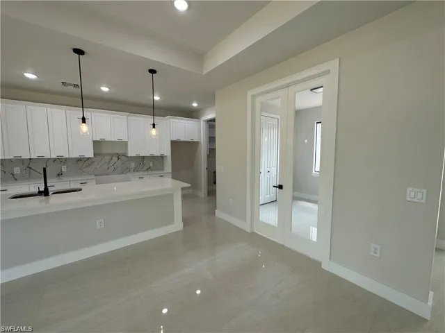 Kitchen featuring light tile patterned flooring, white cabinets, backsplash, hanging light fixtures, and sink