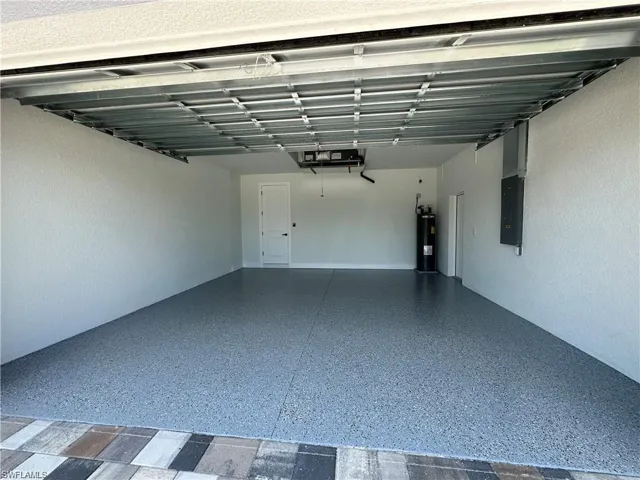 Garage with water heater, electric panel, and a garage door opener