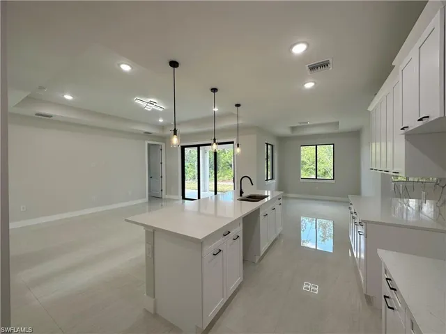 Kitchen featuring light tile patterned floors, white cabinets, hanging light fixtures, a spacious island, and sink