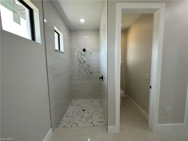 Bathroom with tile patterned floors, toilet, and a tile shower
