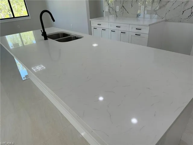 Kitchen featuring white cabinets, sink, light stone counters, decorative backsplash, and light tile patterned flooring