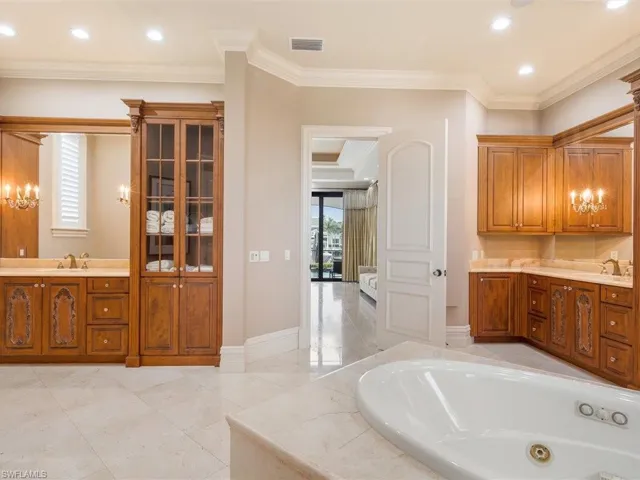 Bathroom featuring vanity, crown molding, a jetted tub, recessed lighting, and light marble finish flooring