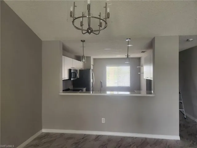 Kitchen with marble finish floor, white cabinetry, stainless steel appliances, baseboards, and a chandelier