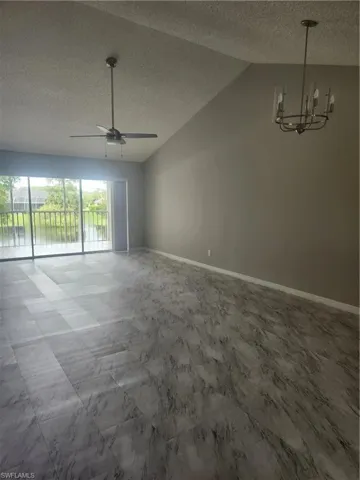 Unfurnished room featuring vaulted ceiling, ceiling fan with notable chandelier, and baseboards