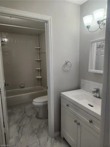 Full bath with marble finish floor, shower / bathtub combination, toilet, and vanity