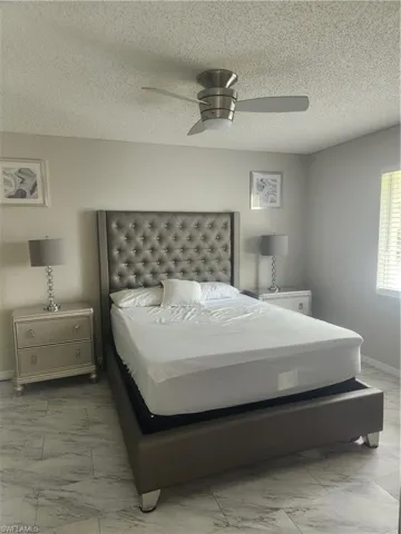 Bedroom featuring baseboards, a textured ceiling, marble finish floor, and a ceiling fan