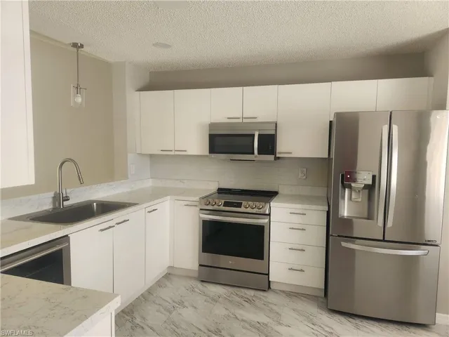 Kitchen featuring decorative light fixtures, appliances with stainless steel finishes, white cabinets, marble finish floor, and a sink
