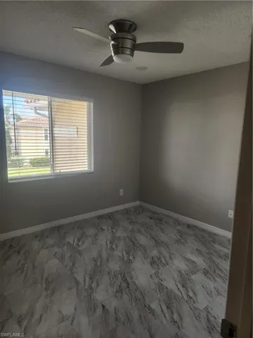 Empty room featuring a ceiling fan, baseboards, marble finish floor, and a textured ceiling