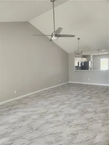 Spare room with baseboards, a textured ceiling, vaulted ceiling, and ceiling fan with notable chandelier